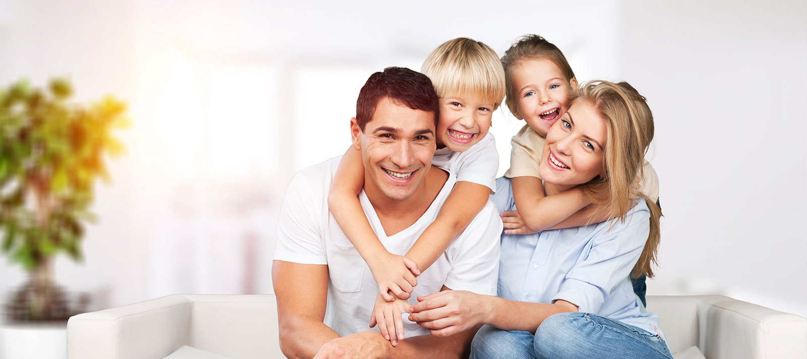 The image shows a family of four posing together on a couch with a cheerful expression, featuring two adults and two children.