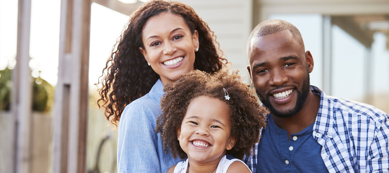 A family photo with a smiling man, woman, and child posing together outdoors during daylight.